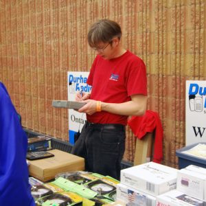 An attendee at the Durham Radio vendor table with Lee, a representative of Durham Radio, making a purchase. 