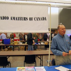 A representative of the Radio Amateurs of Canada (RAC) speaks with an attendee in front of RAC's vendor table.